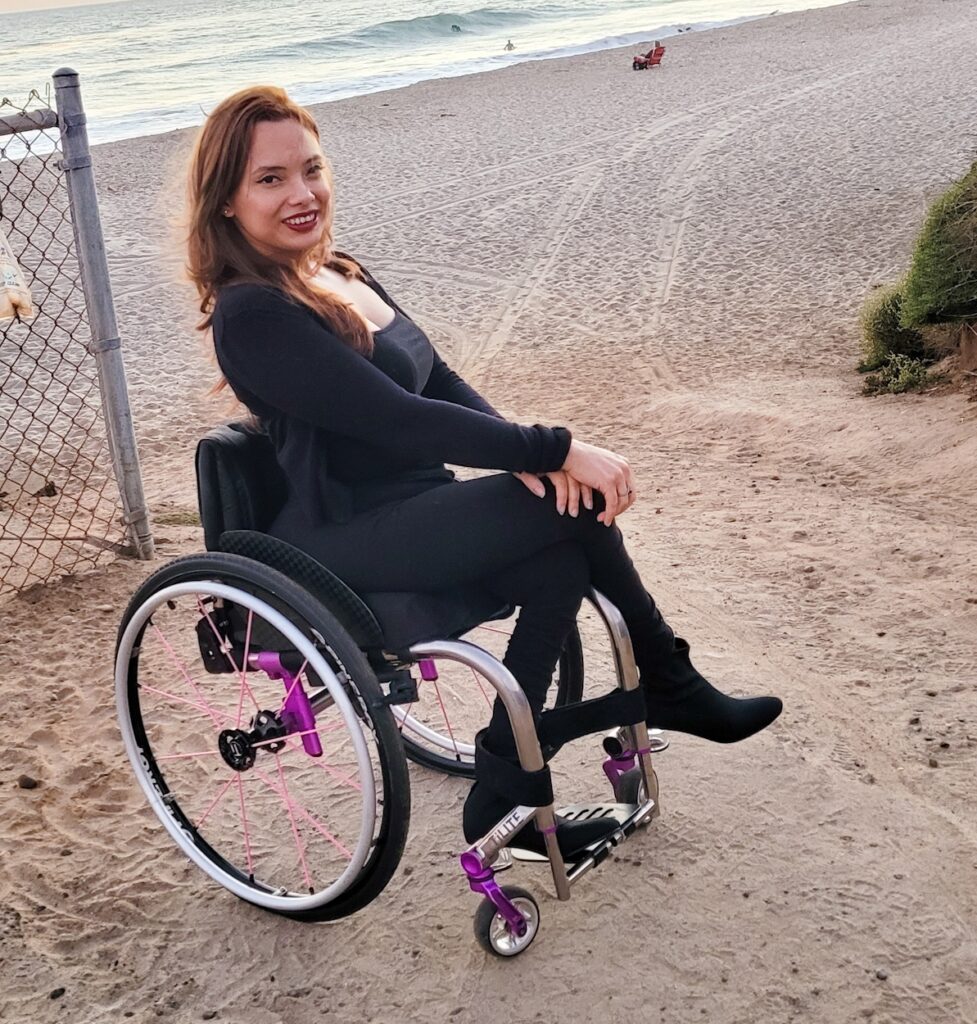 Woman in a wheelchair poses by the beach.